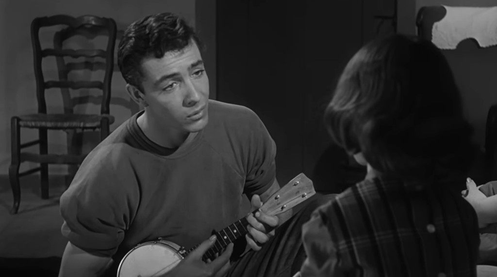 A young man playing a banjo while looking at a young girl in a black and white setting.