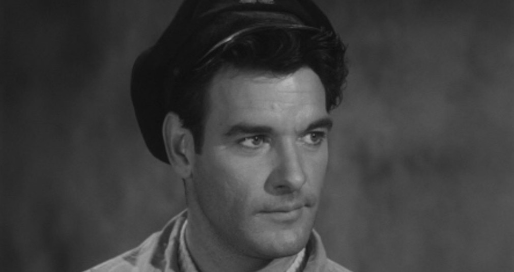 A close-up portrait of a man wearing a cap, looking thoughtfully to the side against a blurred background.