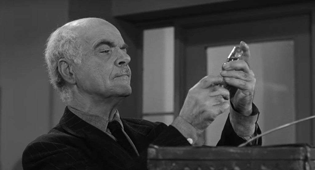 An elderly man with a mustache examines a small object in his hands, appearing focused and contemplative.