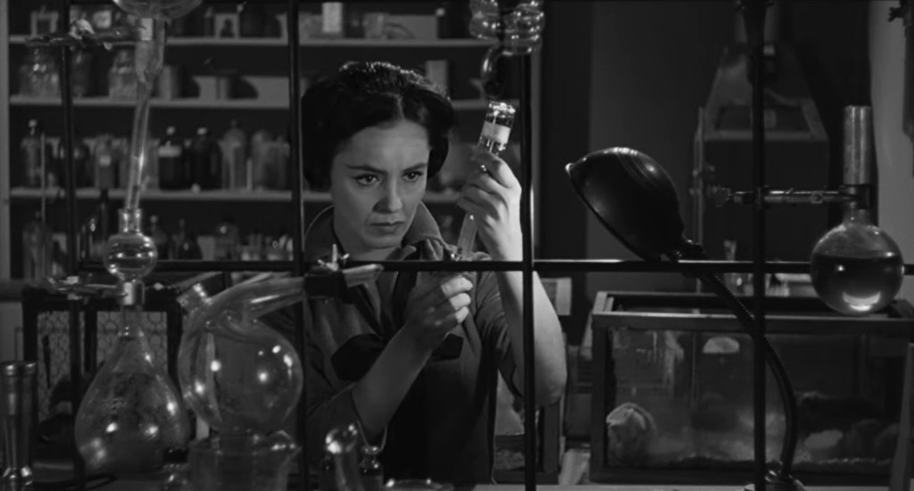 A woman in a laboratory carefully examines a glass vial while surrounded by various scientific equipment and bottles.