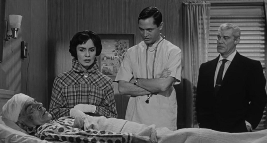 A group of four individuals in a hospital room, with a patient in a bed covered by a blanket. The patient appears to be bandaged and unconscious. A woman in a plaid coat looks concerned, while a doctor in scrubs, alongside another man in a suit, appears to be discussing the situation.