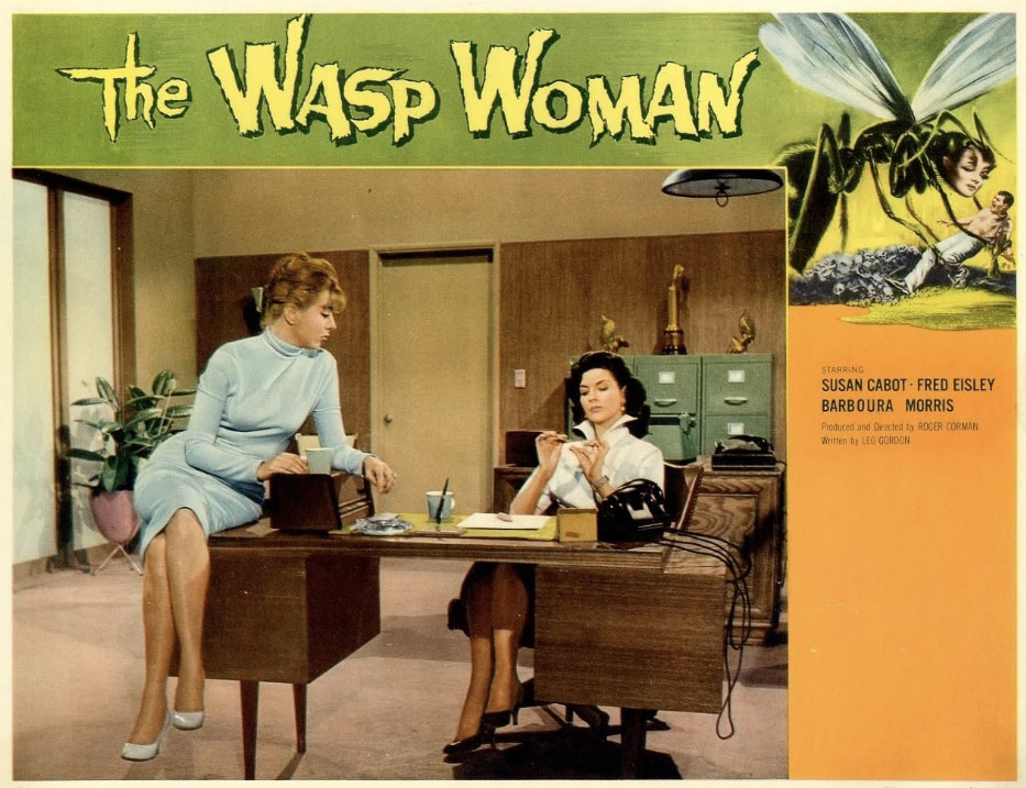 A promotional image for the film 'The Wasp Woman' featuring two women in an office setting. One woman is seated at a desk holding a pen, while the other stands beside her in a blue dress, looking at her with a concerned expression.