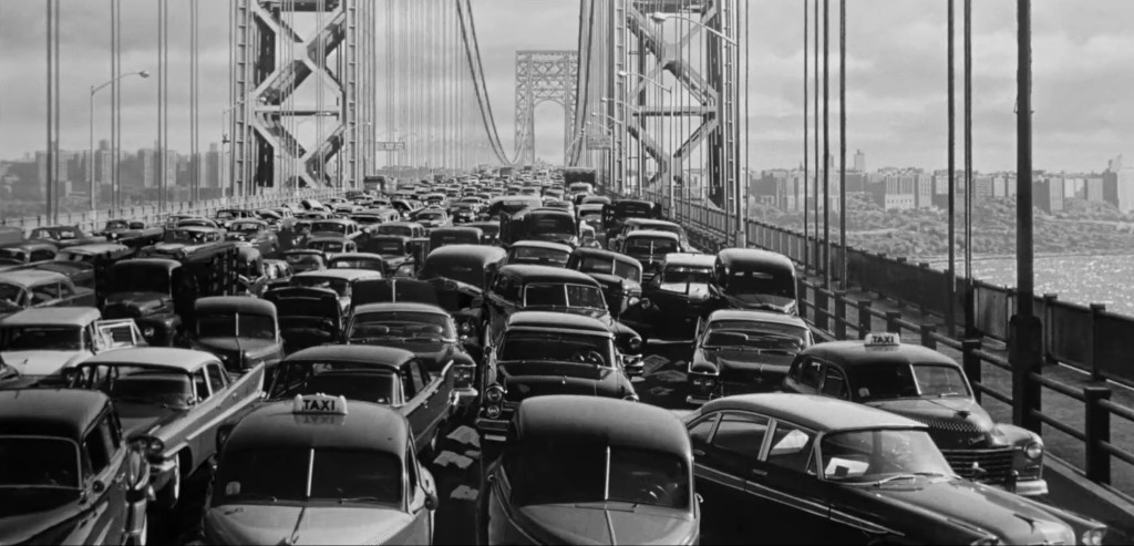 A busy scene of vintage cars stuck in traffic on a bridge, with the George Washington Bridge in the background.