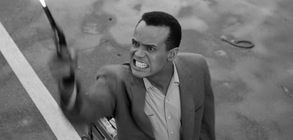 A man in a gray suit, looking angrily upwards while holding a gun. The image is in black and white, capturing an intense moment.