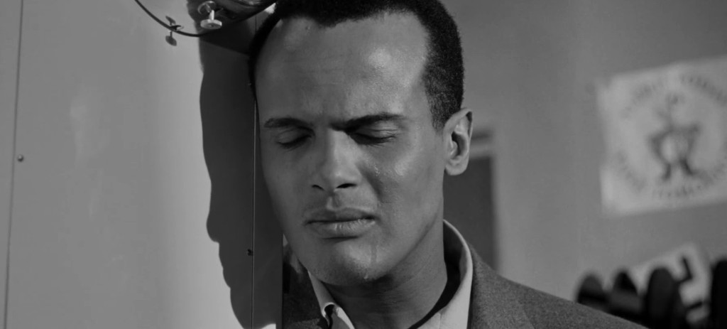 A man with closed eyes leaning against a wall, conveying a sense of contemplation or sadness in a black and white setting.
