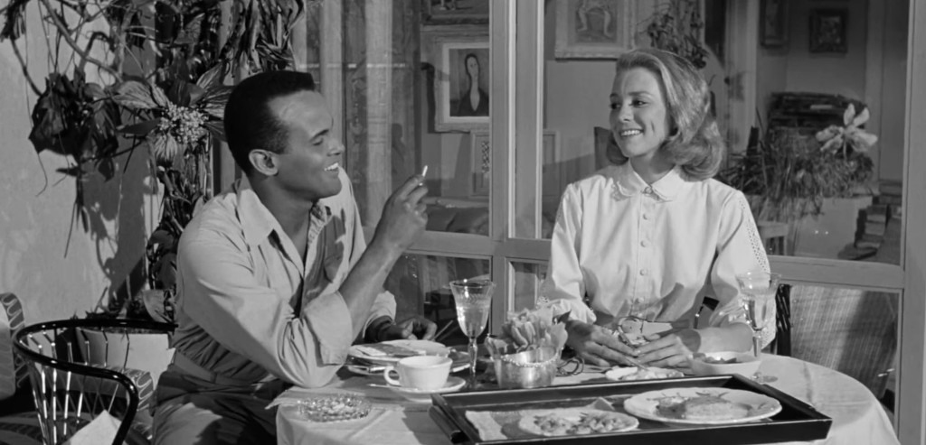 A man and woman enjoying breakfast at a table, smiling and engaging in conversation, surrounded by potted plants and decor.