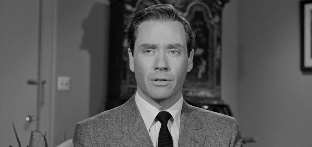 A black and white image of a man in a suit, looking serious and contemplative, with a decorative background.
