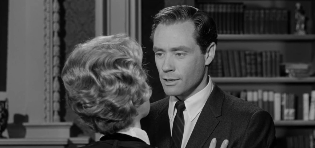 A close-up scene featuring a man in a suit and a woman with styled hair, engaged in an intimate conversation in a vintage setting.