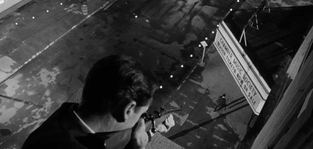A person aiming a rifle from a rooftop, overlooking a street with a marquee sign for 'Chamber Music Society' and a figure walking below.