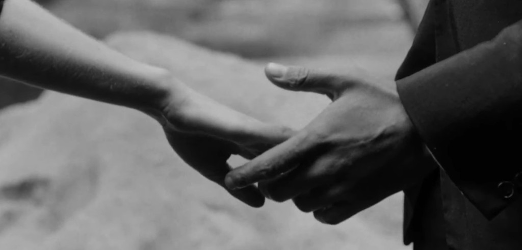 A close-up of two hands reaching out to each other, one belonging to a person in a suit and the other to a person with bare arms, set against a soft blurred background.