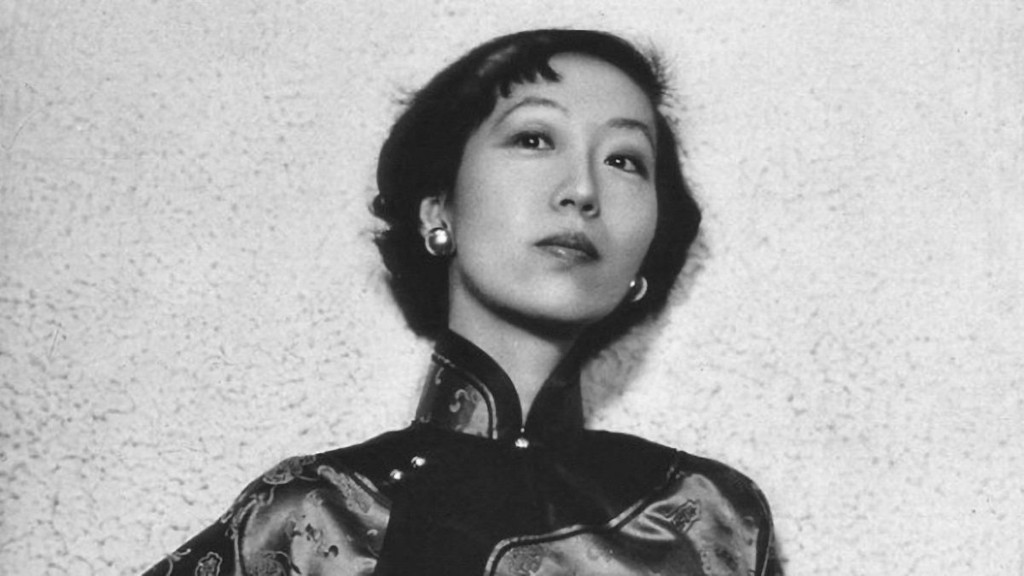 Black and white portrait of a woman wearing a traditional patterned dress, with a confident expression against a textured background.