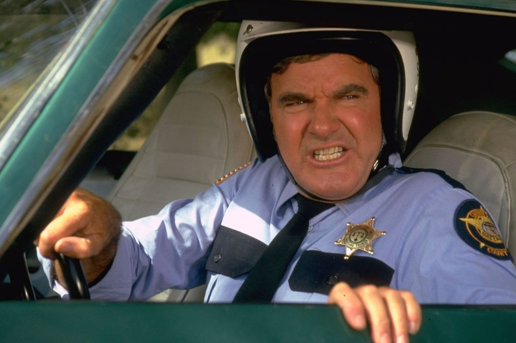 Angry police officer with a stern expression, wearing a helmet, sitting in a car.